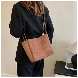 Détail du sac cabas en daim marron porté à l'épaule avec texture mate et style épuré