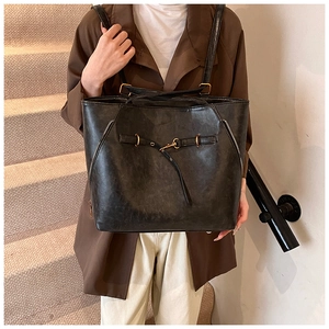 Close-up of black oil wax leather tote bag featuring gold buckle and decorative side zippers