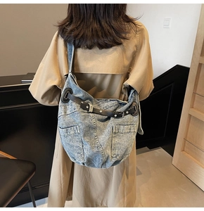 Detail of a large denim hobo bag with black leather straps and silver metal buckles