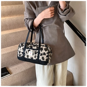 Detail of leopard print plush barrel bag with black leather handle and red heart label