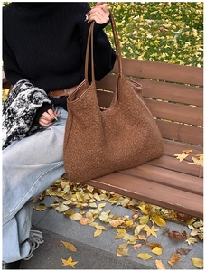 Close-up of brown plush fuzzy tote bag with leather strap on a park bench