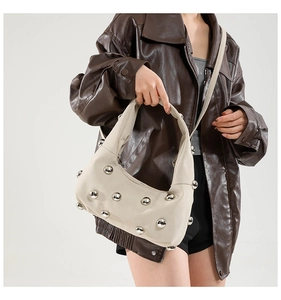Detail of beige crescent underarm bag featuring large silver metal ball embellishments