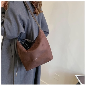 Detail of soft brown suede hobo bag with white printed text and adjustable shoulder strap