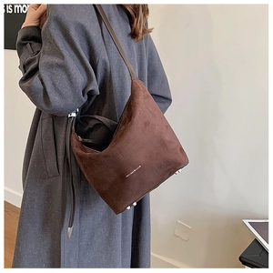 Brown suede hobo bag with adjustable strap and metal protective feet on a side-view model