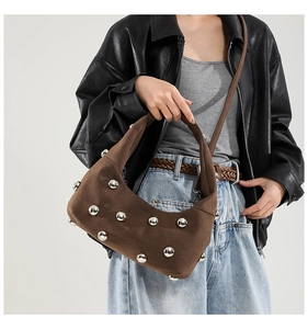 Detail of dark brown suede crescent bag featuring silver stud rivets and a slim strap