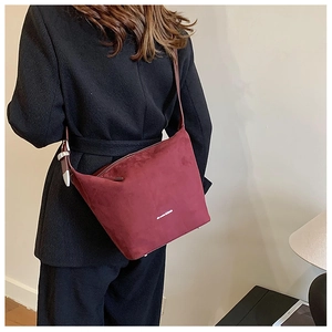 Detail view of burgundy faux suede bucket bag with silver buckle worn by a model
