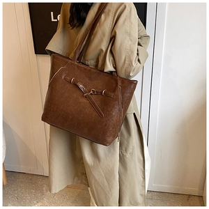 Close-up of vintage brown leather tote bag showing buckle detail and metal eyelets on shoulder