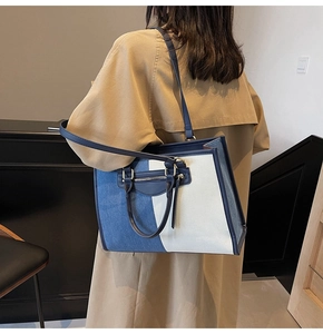 Detail of navy denim and beige canvas patchwork tote bag worn by a model in lifestyle setting