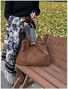 Close-up of brown faux shearling tote bag with leather straps on park bench in autumn