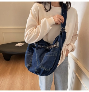Detail of a large dark blue denim hobo bag featuring functional pockets and black leather straps