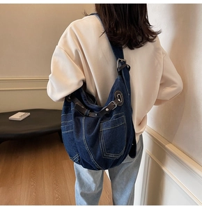 Detail of dark blue denim hobo bag featuring brown leather straps and yellow stitching