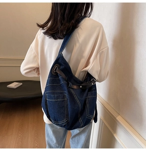 Detail of dark denim hobo bag featuring yellow contrast stitching and leather shoulder strap