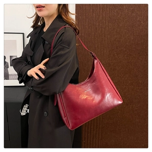 Detail view of burgundy PU leather handbag with metallic logo worn by a model
