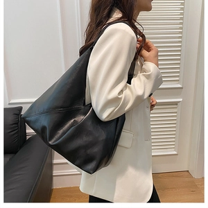 Side view of a large black leather tote bag worn by a model in a white suit