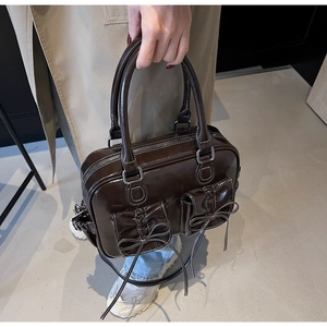 Detailed view of dark brown patent leather handbag with white stitching and bow accents
