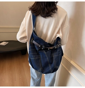 Detailed view of large dark blue denim crossbody bag with front pockets and leather straps