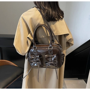 Detail of dark brown leather handbag with white stitching and bow-tie front pockets