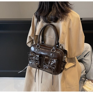 Detail of dark brown glossy leather shoulder bag featuring bow pockets and retro style