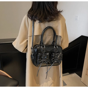 Detail of black bow handbag with white contrast stitching on model in modern hallway