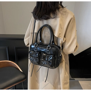 Detail of black glossy shoulder bag with bow accents and silver hardware on a trench coat