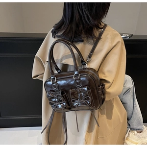 Detail view of a coffee brown glazed leather backpack worn over a khaki trench coat