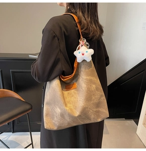 Detail of a large brown tote bag with star pendant, shown worn as a shoulder bag