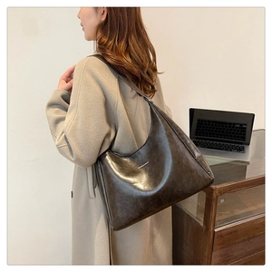 Detail of a large brown faux leather hobo bag with a silver brand logo on the side