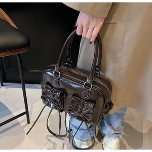 Detail of glossy brown Boston bag with bow pockets shown on a model in trench coat