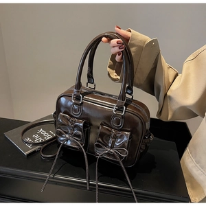 Detail of dark brown glossy leather handbag with bow pockets and white contrast stitching