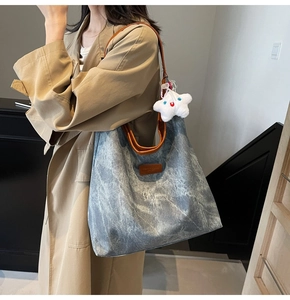 Detail view of large denim tote bag with brown leather handles and star charm