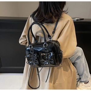 Detail showing shiny black leather crossbody bag with white stitching and bow accents