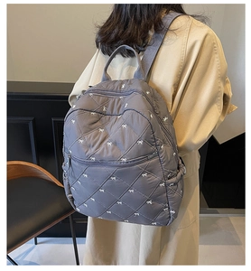 Close-up of gray quilted backpack featuring white bow embroidery and front pocket detail
