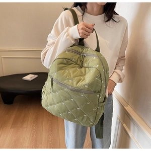 Close-up of quilted light green fabric with fine white bow embroidery and zipper details