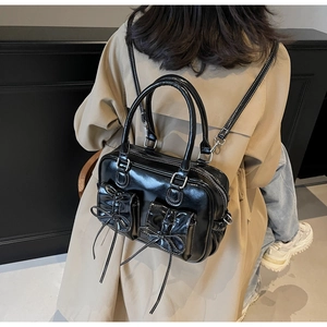 Close-up of black patent leather backpack with bow-decorated pockets and white stitching