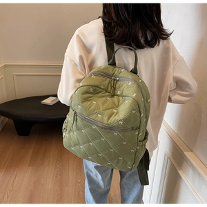 Detail of green quilted backpack featuring white bow embroidery and diamond stitching