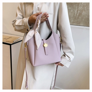 Detail of lavender lychee leather bucket bag with gold lock and decorative silk scarf
