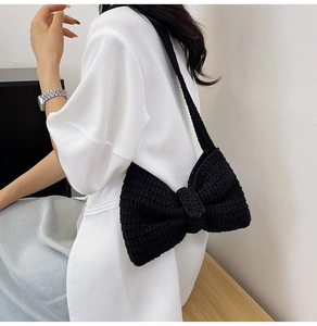Sac à bandoulière noir en tricot fait main avec un grand nœud porté par un mannequin