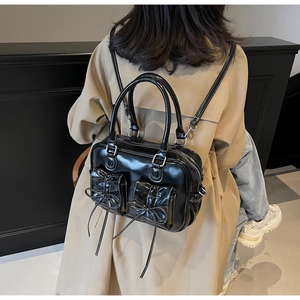 Black patent leather backpack with white stitching and bow detail shown on a model