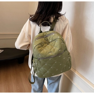 Detail showing olive green quilted backpack with white bow embroidery in lifestyle setting
