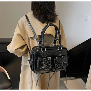 Model wearing a black glossy patent leather backpack with bow-tied pockets and white stitching
