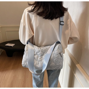 Detail of light blue flower-quilted crossbody bag with wide adjustable strap on shoulder