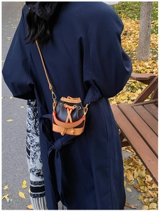Mini sac seau avec cordon et garniture dorée porté par un mannequin en automne