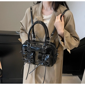 Detail of black patent leather crossbody bag with bow pockets on a trench coat model