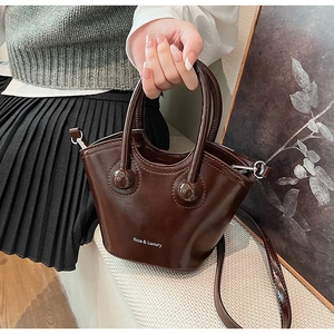 Detail of dark brown leather bucket bag featuring glossy finish and luxury branding
