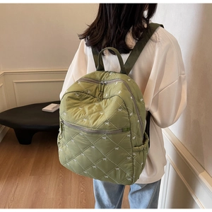 Close-up of green diamond quilted backpack with white bow prints and multi-pocket detail