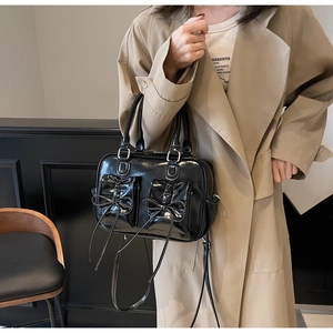 Detail view of black glossy leather bag with bow knots and dual front pockets