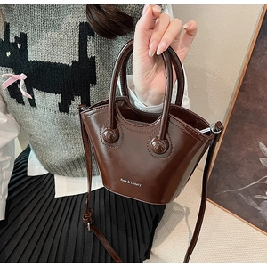 Detail of dark brown leather bucket bag with top handles and adjustable shoulder strap