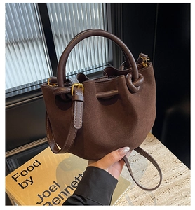 Detail view of brown suede bucket bag featuring drawstring closure and gold metal hardware