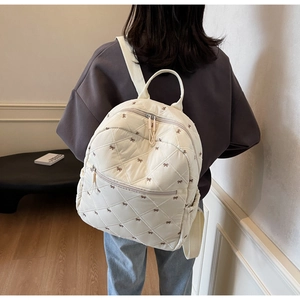 Rear view of a cream quilted backpack with brown bow embroidery on a female model