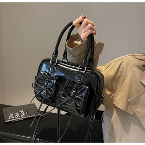 Close-up of black patent leather handbag with bow details and functional double front pockets